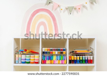 Transparent plastic containers with stationery and supplies for drawing and craft on shelves. White shelving with various material for creativity and art activity. Organizing and storage craft room.  Royalty-Free Stock Photo #2277590031