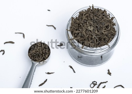 Leafy black tea next to a metal spoon on a white background
