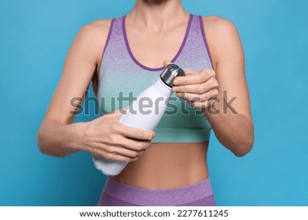 Sportswoman with thermo bottle on light blue background, closeup