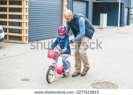 Father teaching his little daughter to ride a bicycle. Child learning to ride a bike. Family activities together.