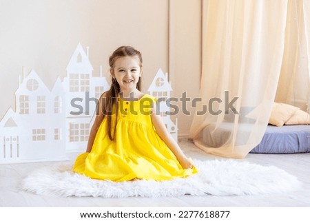 Little cute girl in yellow dress plays in the bright children's room. Funny cute little girl having fun in the children's room.