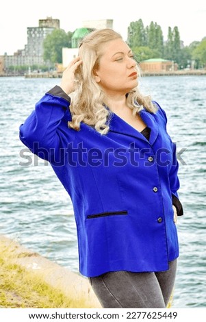 Blonde plus size model wearing blue jacket nature water background travelling travel posing in nature blog glamout fashion article