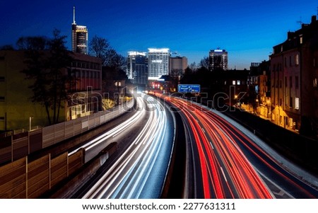 Curved Motorway A40 called “Ruhrschnellweg“ at blue hour after sunset in Essen City Ruhr Basin Germany with six lanes, bright light traces, sky gradient and skyline silhouettes of office towers. Royalty-Free Stock Photo #2277631311