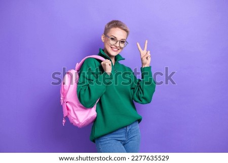 Photo of good mood blonde short hair lady wear green jumper hold new pink stylish school backpack show v-sign isolated on purple color background