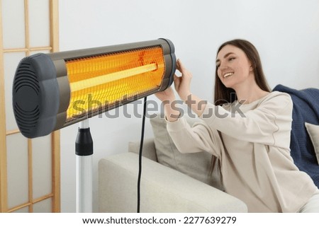 Woman adjusting temperature on electric infrared heater indoors Royalty-Free Stock Photo #2277639279