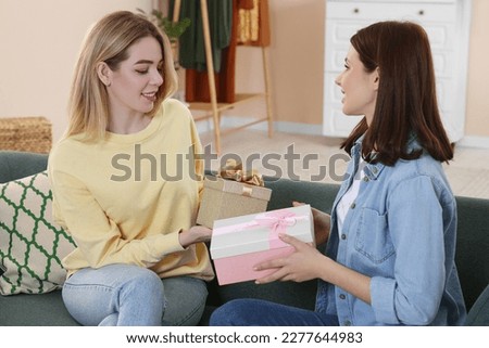 Smiling young women presenting gifts to each other on sofa at home