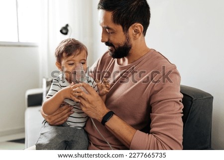 Portrait of a baby boy inhaling medicine in nebulizer with his father at home. Royalty-Free Stock Photo #2277665735
