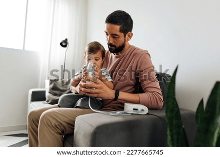 Portrait of a baby boy inhaling medicine in nebulizer with his father at home. Royalty-Free Stock Photo #2277665745