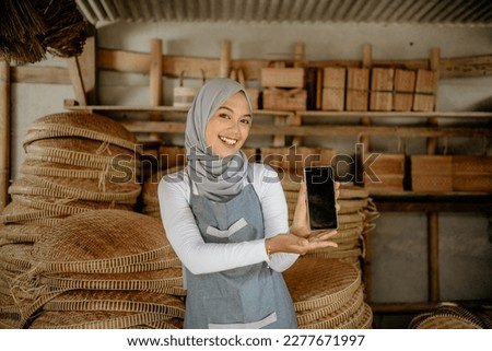muslim beautiful woman showing her phone screen to camera while standing in her handicraft shop