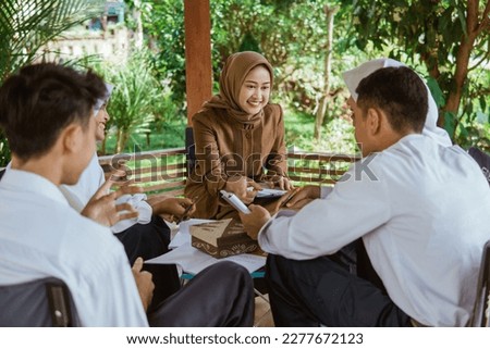 teacher in Veil guides students to do the questions in the book in the gazebo during outdoor class Royalty-Free Stock Photo #2277672123