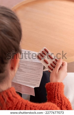 Young female with pills sitting in light room near coffee table and reading medicament package insert Royalty-Free Stock Photo #2277677073