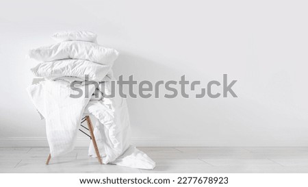 dirty blanket, linen bedding, cotton sheets, cushions and duvet with natural material on chair on white wall background with copy space, washing concept  Royalty-Free Stock Photo #2277678923