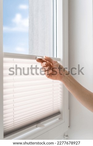 cropped shot of female hand pull and close pleated jalousie on window in living room, controlling lighting range, protection of sunlight, closeup Royalty-Free Stock Photo #2277678927