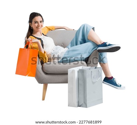 Cheerful happy shopaholic woman with lots of shopping bags, she is sitting on an armchair and celebrating with arms raised Royalty-Free Stock Photo #2277681899
