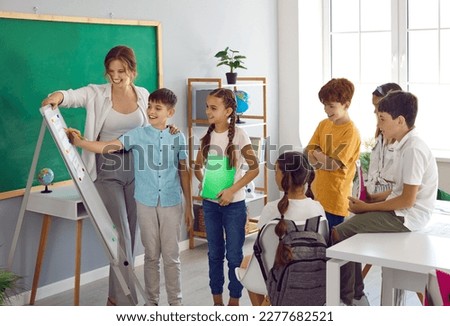 Classmates work together on school project. Elementary school students use whiteboard together with the teacher during lesson. Children take turns writing on whiteboard. Learning and school concept. Royalty-Free Stock Photo #2277682521