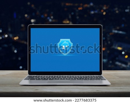 Home with shield flat icon on modern laptop computer monitor screen on wooden table over blur colorful night light city tower and skyscraper, Business home insurance and security online concept