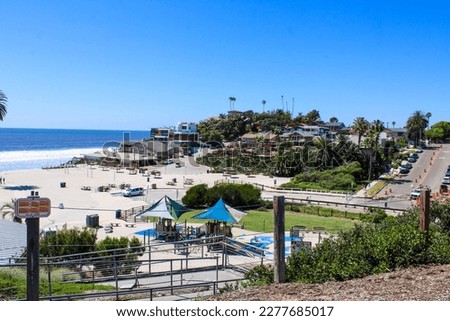 gorgeous shot of the blue ocean water, lush green palm trees and beach houses with people walking along the beach at Moonlight State Beach in Encinitas California USA Royalty-Free Stock Photo #2277685017