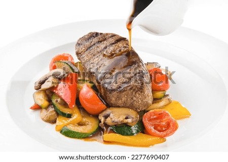 The chef pours sauce over the steak. A piece of steak with grilled vegetables and sauce