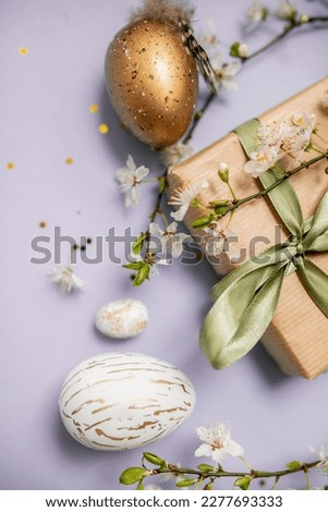 beautiful light easter layout with eco-wrapped gifts, golden and marble eggs, cherry blossoms and confetti on a pastel purple background. top view. copy space. flat lay. place for text