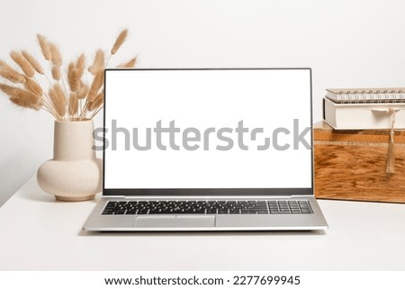 Mockup laptop with white screen on the table with vase, lagurus grass, wooden box with books. Aesthetic background for study, cozy home office, website promotion, branding and social media template