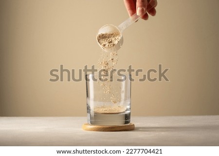 Pouring protein powder from scoop, in glass a glass. Making protein drink. Royalty-Free Stock Photo #2277704421