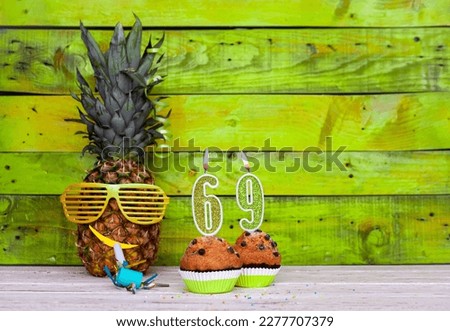 Creative card postcard happy birthday with number  69. Background character pineapple in festive glasses. Copy space anniversary card on yellow colorful wooden background.