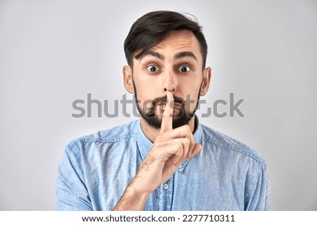 Portrait of young caucasian man covering his mouth with finger isolated on white background. Asks for silence, keep secret, shh gesture
