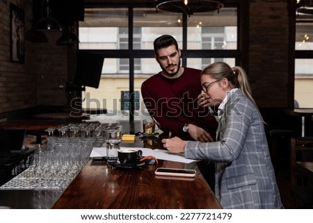 Health inspector sitting in a restaurant and writes a fine and a negative report to the owner or manager of the cafeteria after she finds poor hygiene conditions in the kitchen. Sanitary inspection