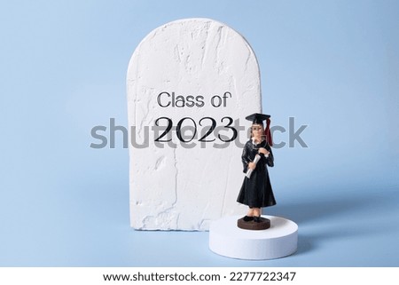 Class of 2023 text and statuette of a graduate in graduate cap and gown on podium stage.