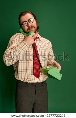 Portrait of retro mature man with moustache and beard in eyeglasses in vintage fashion clothes talking on phone over dark green background. Concept of retro style, emotions, business, work