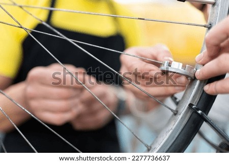 close-up detail of inexperienced hand using trixes, spoke spanner to align the wheels of a bicycle, behind other woman's hands explaining how to perform the work and maintenance of the bicycle wheel. Royalty-Free Stock Photo #2277736637