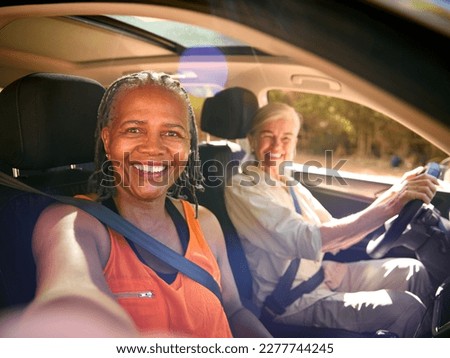 POV Shot As Passenger Takes Selfie On Phone As Two Senior Female Friends Enjoy Day Out In Car