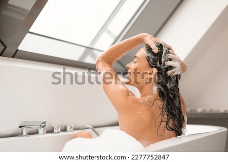 Haircare Cosmetics. Lady Applying Shampoo On Long Hair Washing Head Sitting In Bathtub Full Of Foam Indoors. Side View Shot Of Happy Woman Enjoying Hair Care Routine In Modern Bathroom Royalty-Free Stock Photo #2277752847