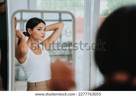 Bored young  pretty Asian woman in white t-shirt and beige pants standing at mirror, tired. Attractive Korean girl frustrated after divorce at home. Fashion fit model. Beauty and health care.