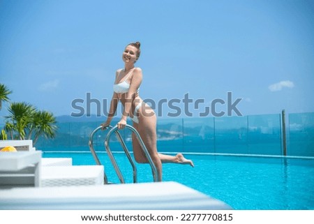 Young beautiful woman lay on sunbed near swimming pool at summer sunny day, enjoy vacation at tropical resort and smile in bikini, sunbathing, tanning 