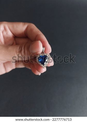 female hand holding heart shaped pendant with blue gemstone
