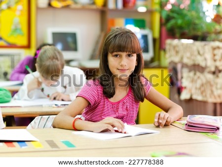 Cute little girl sitting in the classroom and smiling. Elementary age. Other kids in the background.