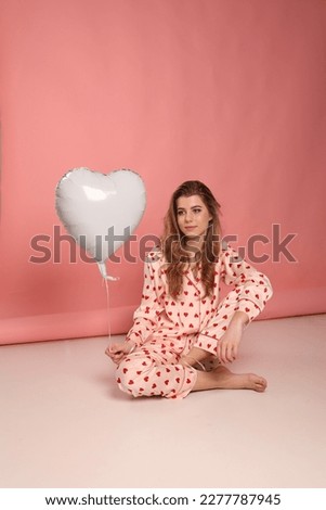 a girl in heart-print pajamas on a pink background with a white heart-shaped gel ball. valentine's day clothes for home and sleep. pajama party