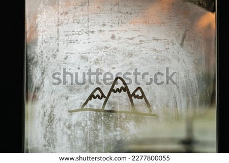 Finger drawing of mountains on a misted window glass.