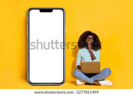 Full length photo of minded pretty person hand touch chin look empty space huge phone isolated on yellow color background