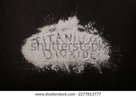 Titanium dioxide powder scattered on black surface with inscription TITANIUM DIOXIDE.  Food coloring, E171. White powder. Pigment present in of paint, food, toothpastes,  and cosmetic products. Royalty-Free Stock Photo #2277813777