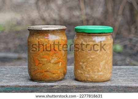 two closed glass jar with red yellow canned salad stand on a gray table in the street