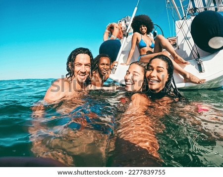 Happy multiracial friends doing selfie swimming in the sea with sail boat in background - Soft focus on center girl face - Summer and travel concept Royalty-Free Stock Photo #2277839755