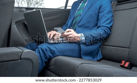 ELEGANT EXECUTIVE OR BUSINESSMAN IN BLUE SUIT WORKING IN THE CAR USING LAPTOP AND SMARTPHONE. BUSINESS TRAVELS CONCEPT. Royalty-Free Stock Photo #2277853029