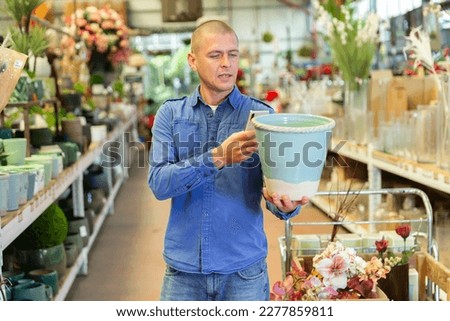 Caucasian man photographing ceramic pot while shopping in home goods store.
