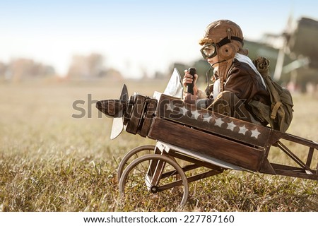 Young Aviator sits in his makeshift toy airplane on airport parking Royalty-Free Stock Photo #227787160