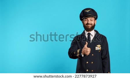 Aviation male pilot giving thumbs up on camera, expressing good sign and approval. Aircrew captain with flying uniform showing agreement and accept, doing okay symbol in studio.