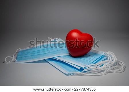 Red heart place over blue surgical masks stacked in layers on gray background, Bacteria protection concept.