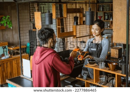 the female barista smiling while receiving the credit card from the customer during the transaction on the cashier desk