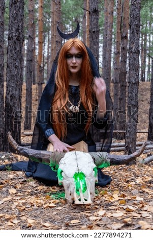 a girl in a Gothic image for Halloween is sitting in the forest with a cow's skull in the autumn forest in the background is a pine forest